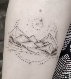 a black and white photo of mountains with stars in the sky on a woman's arm