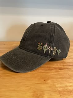 a black hat with cactus embroidered on the side sitting on a wooden table next to a white wall