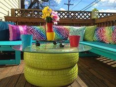 a table made out of old tires on a deck with colorful pillows and flowers in vases