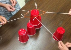 several children are playing with red cups on a wooden table and stringing them together