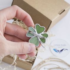 a person holding a four leaf clover brooch in their hand next to a box