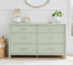 a green dresser in a white room with a round mirror on the wall