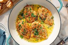 a pan filled with chicken covered in sauce and parmesan bread on the side