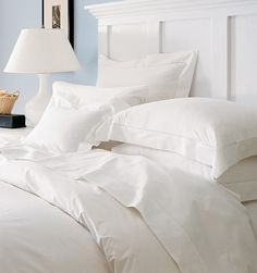 a bed with white sheets and pillows next to a lamp on a nightstand in a bedroom