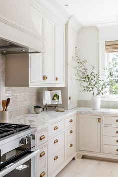 a kitchen with white cabinets and marble counter tops, gold pulls on the oven door