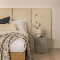 a white bed with pillows and blankets on top of it next to a tall plant