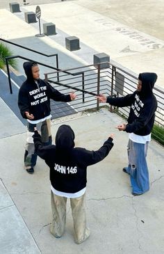 four young men in hoodies are standing on the sidewalk and pointing at each other