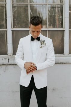 a man in a white tuxedo and black bow tie looking down at his watch