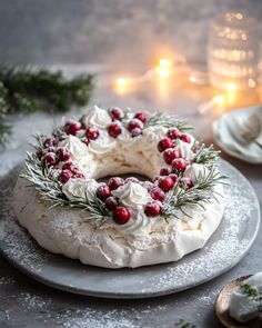 a cake decorated with white frosting and cranberries on a plate next to candles