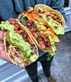 a person holding two tacos with guacamole and tomatoes