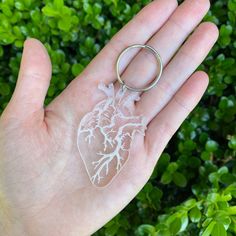 a hand holding a clear heart shaped keychain in front of green bushes and shrubbery