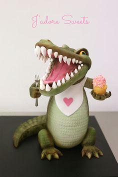 a toy alligator holding a cupcake with its mouth wide open and teeth wide open