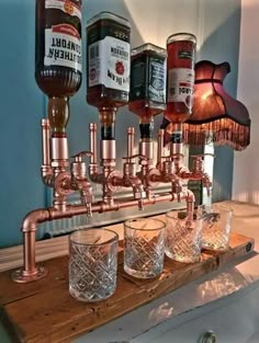 a wooden table topped with glasses filled with liquor next to a wall mounted faucet