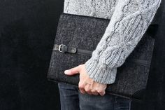 a person holding a black laptop bag in their left hand and wearing a gray sweater