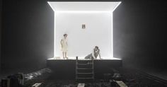 two people standing in front of a white wall with light coming through the window and another person sitting down