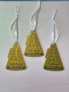 three yellow triangle shaped tags with white ribbons hanging from each one's neckline