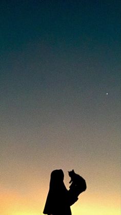 a woman holding a cat in her arms at sunset with the moon visible behind her