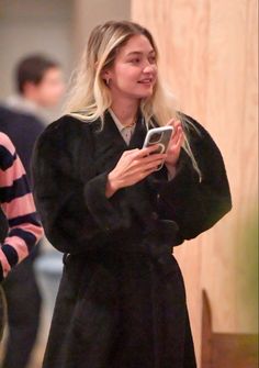 a woman in a black coat looking at her cell phone while standing next to another person