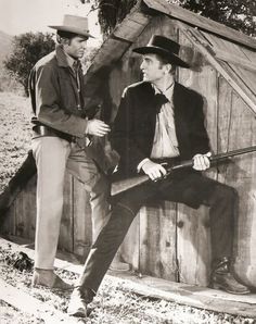 black and white photograph of two men sitting on a wooden bench in front of a fence