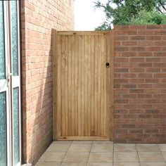 an open wooden door on a brick wall next to a tiled floor and tree in the background