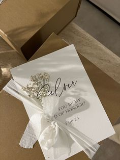 an open box with a wedding card and flower on it, sitting on the floor