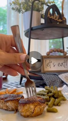 a person is holding a fork over some food on a plate with green beans and potatoes