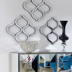 a mirrored cabinet with three decorative mirrors on the wall above it and a vase next to it