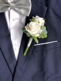 a boutonniere with a white rose and green leaves on the lapel