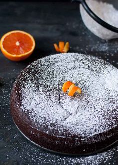 a chocolate cake covered in powdered sugar with an orange slice on the plate next to it