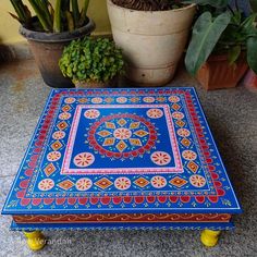 a blue and red table sitting on top of a floor next to potted plants