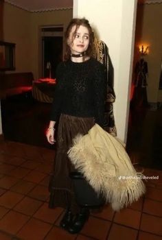 a woman standing in a room holding a large furry handbag and looking at the camera