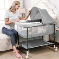 a woman sitting on a bed next to a baby bassinet and changing table