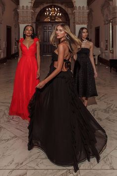 three models in black and red gowns walk down the runway