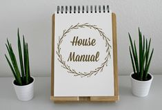 a house manual sitting on top of a desk next to two potted plants and a notepad