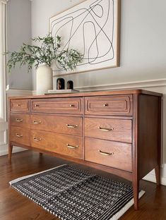 a wooden dresser sitting on top of a hard wood floor next to a plant in a vase