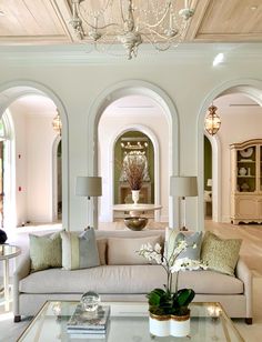 a living room filled with furniture and a chandelier above a glass top coffee table