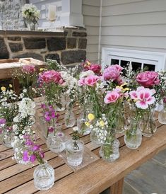 a wooden table topped with lots of glass vases filled with flowers on top of it