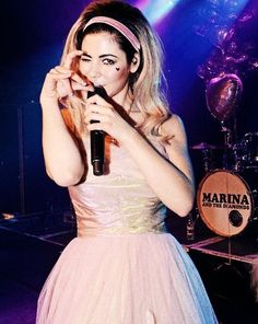 a woman in a pink dress is holding a microphone and singing into the microphone on stage