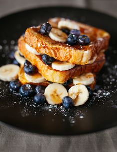 some bananas and blueberries are stacked on top of each other in a black plate