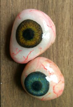 two painted rocks with an eye on them sitting on a wooden table next to each other