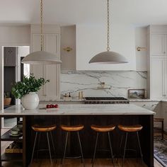 a kitchen with marble counter tops and stools in front of an island that has three pendant lights hanging from the ceiling