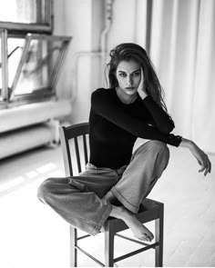 a black and white photo of a woman sitting on a chair with her hands behind her head