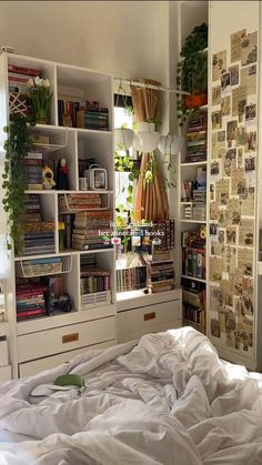 an unmade bed in a bedroom with many bookshelves and plants on the wall