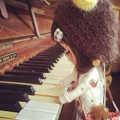 a doll is playing the piano with a teddy bear in her hand and wearing a hat