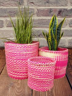 three pink and white baskets sitting on top of a wooden table next to a green plant