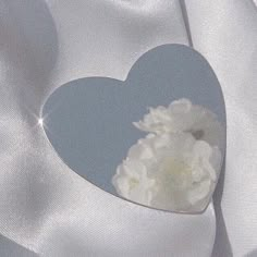 a heart - shaped box filled with white flowers on top of a silver satin fabric