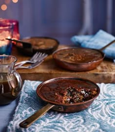 two bowls of food on a table next to a glass pitcher and tea pot with a candle in the background