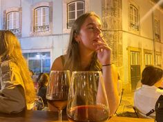 a woman sitting at a table with two wine glasses in front of her and another person standing next to her