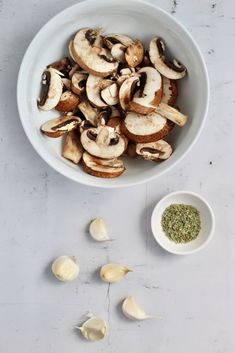 sliced mushrooms in a white bowl next to garlic and seasoning