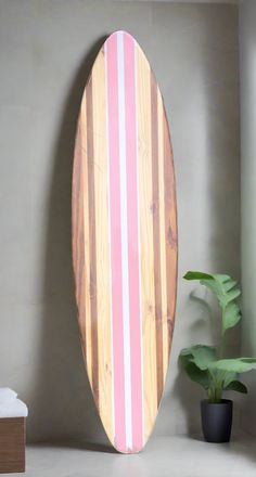 a pink and white striped surfboard next to a potted plant